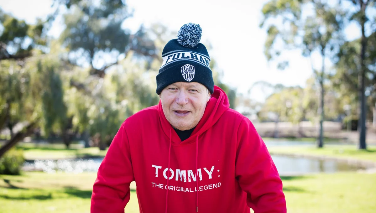 A portrait of participant Tommy wearing a black and white knitted hat and a read sweatshirt with the words 'Tommy'.