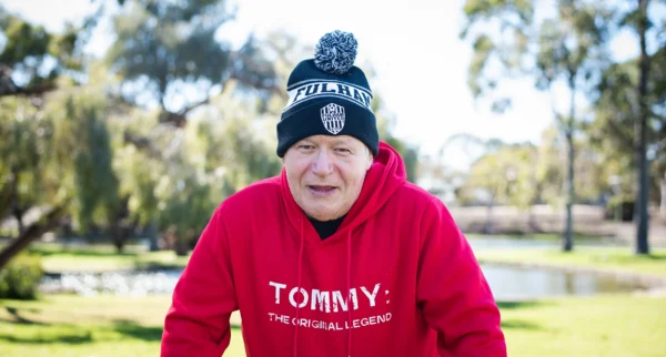A portrait of participant Tommy wearing a black and white knitted hat and a read sweatshirt with the words 'Tommy'.
