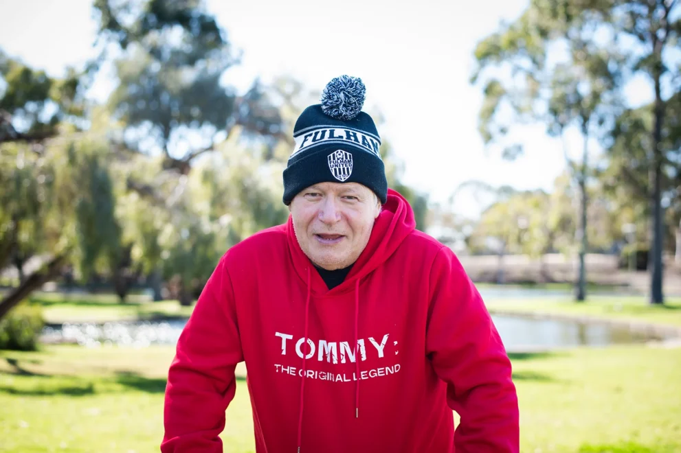 A portrait of participant Tommy wearing a black and white knitted hat and a read sweatshirt with the words 'Tommy'.