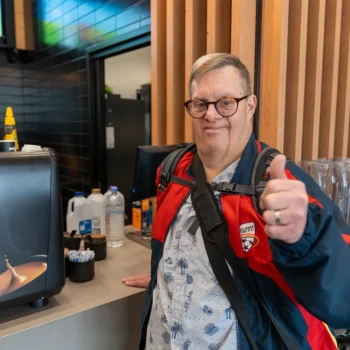 Participant Nick on his way to work. He is getting a beverage at a local cafe and smiling with a thumb's up.