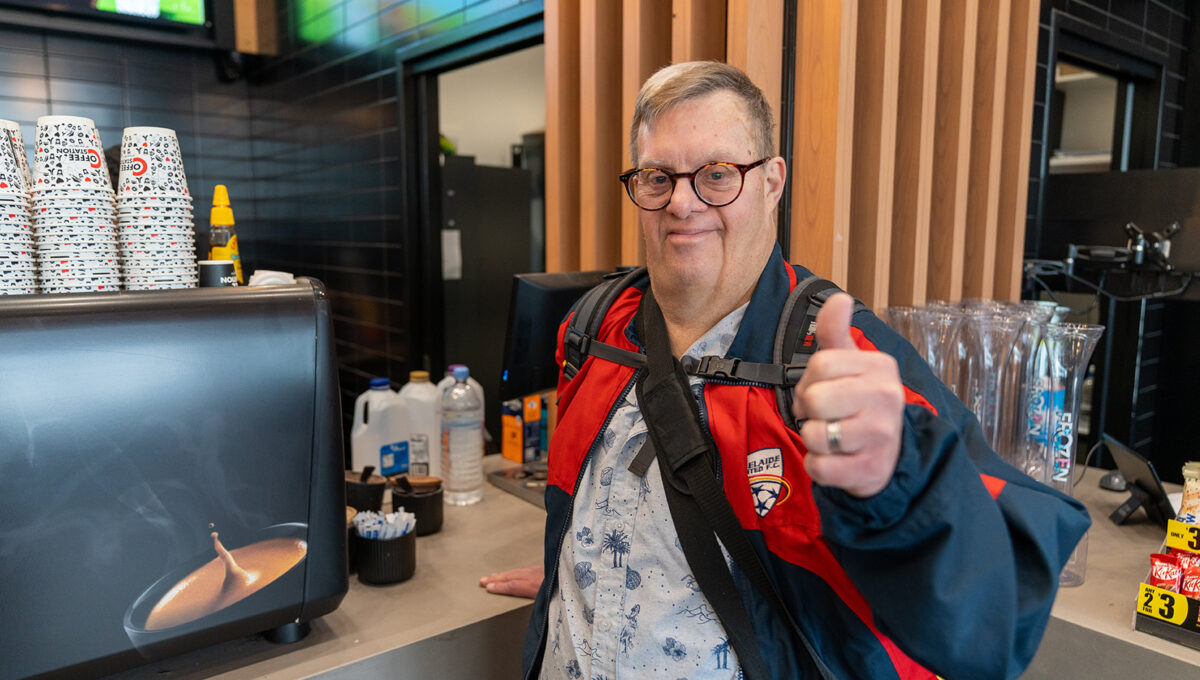 Participant Nick at a cafe counter smiling with a thumbs up.