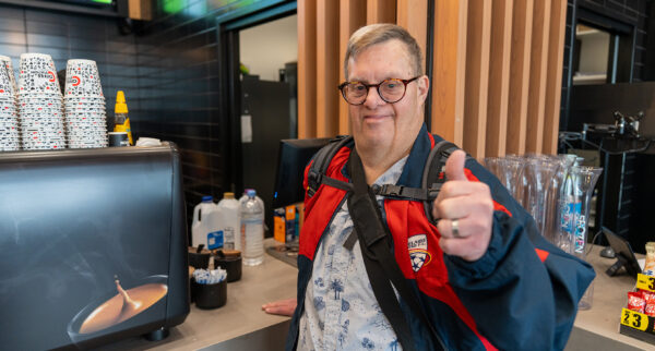 Participant Nick at a cafe counter smiling with a thumbs up.