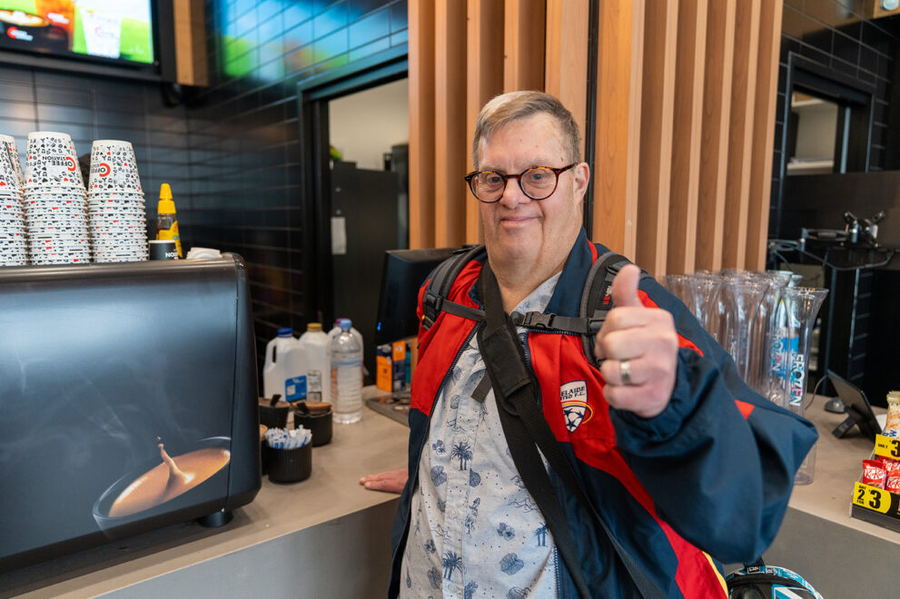 Participant Nick at a cafe counter smiling with a thumbs up.